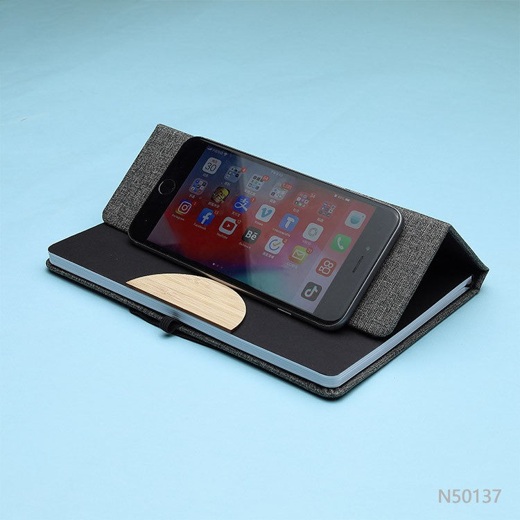 Cuaderno porta celular de tela R-PET y detalle en bambú, disponible en colores gris o negro. Logotipo en grabado láser en la tapa.